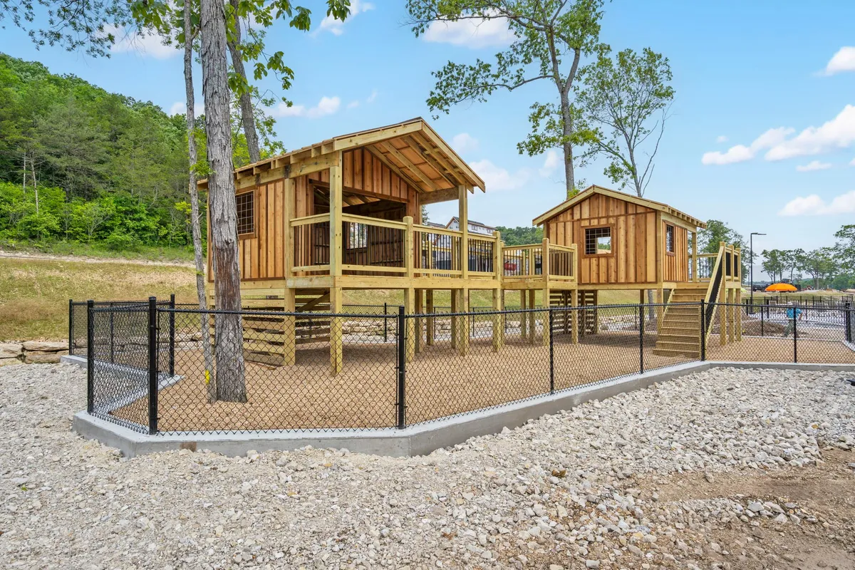 This image features vibrant playground structures set amidst lush greenery within a fenced area. Children are seen playing and families are gathered for outdoor fun, creating a lively, welcoming atmosphere ideal for family outings and celebrations.