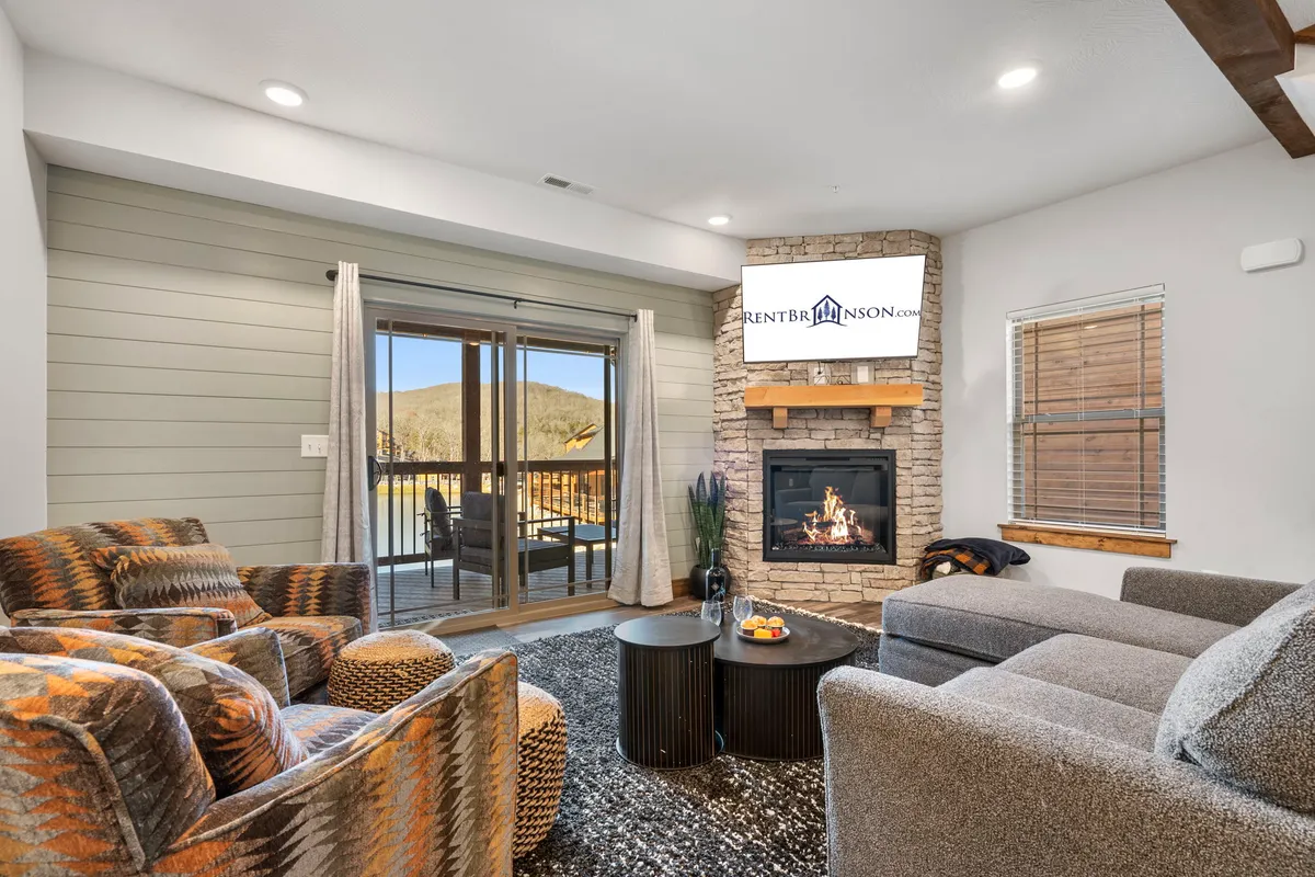 A living room styled with a cozy fireplace, large windows that fill the room with natural light, and comfortable seating. The view outside connects the indoor space to the natural surroundings, while the arrangement encourages relaxation and social moments.