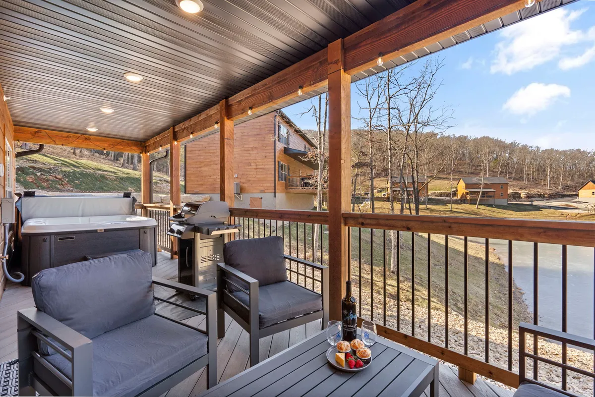 An inviting exterior scene showing an outdoor seating area with a hot tub, grill, food and wine setup, and scenic lake views. The grill and food setup hint at alfresco dining opportunities, while the outdoor environment emphasizes relaxation and memorable gatherings.