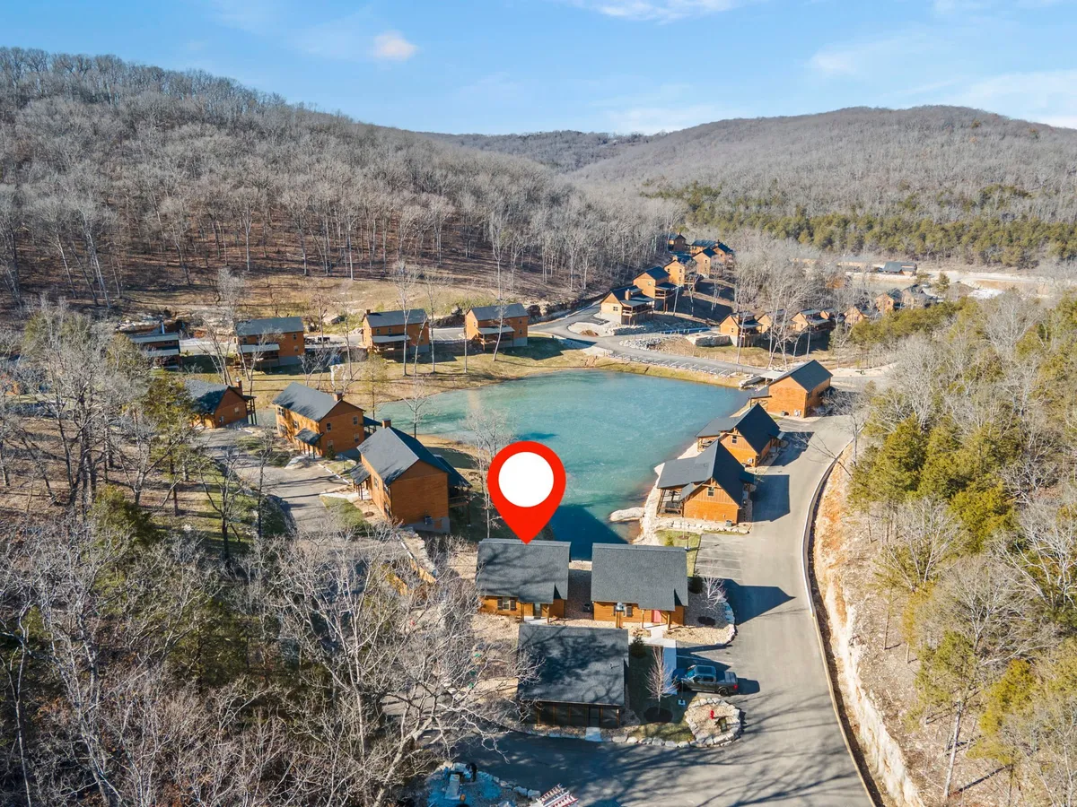 Several cabins are nestled among trees near the lake, with a road leading to the water and communal outdoor spaces visible. The environment is peaceful and communal, perfect for family gatherings and nature exploration.