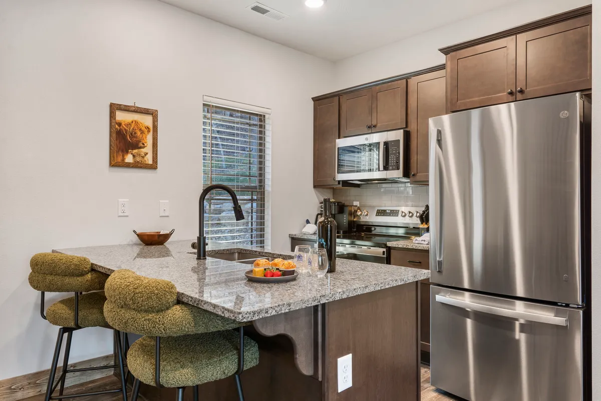 This image captures a modern kitchen with granite countertops, a colorful fruit platter, sleek modern appliances, and stylish bar stools. The scene is bright and welcoming, inviting both meal prep and casual dining.