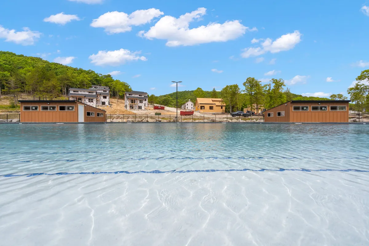 This image features several waterfront cabins set against clear blue water and distant forested hills. A construction area is visible in the background, hinting at the ongoing development within the community. The scene radiates a feeling of tranquility and exclusivity, with only a few cabins and open space.