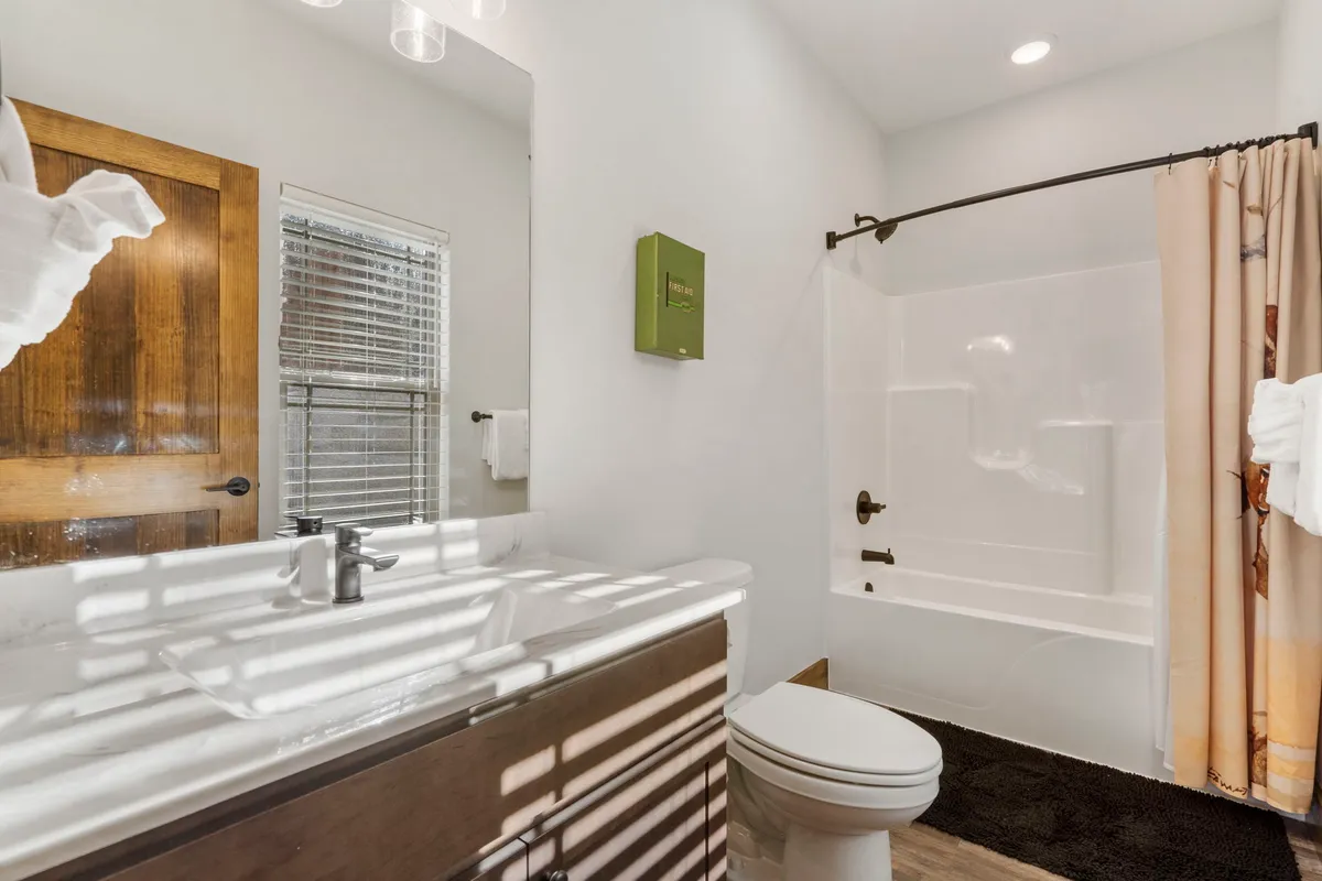 A modern bathroom featuring a large vanity with sink, expansive mirror, bathtub, and shower curtain on a dark rug. The space is bright and fresh, inviting moments of relaxation and personal care.